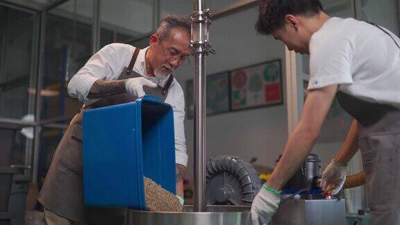 亚洲华人工人将生咖啡豆装入咖啡烘焙机为咖啡烘焙过程做准备