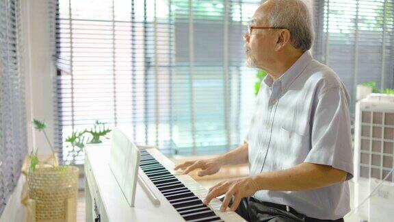 一位头发花白的亚洲老人在休息时间下班后在自家客厅练习弹钢琴