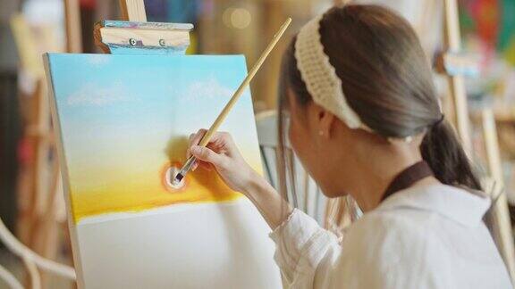 年轻的亚洲女艺术家在艺术工作室画日落风景画