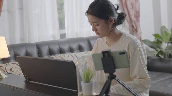 中等shota亚洲青少年在家里的客厅里弹奏键盘钢琴美丽的女孩钢琴家在社交媒体上直播弹钢琴网络影响者Vlog或网络教学