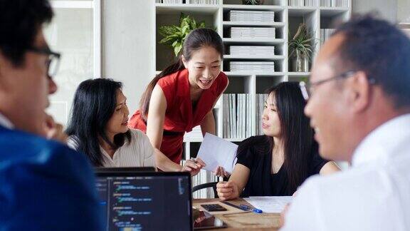 (中景)两个女人在忙碌的办公室聊天时一个同事走近了她们