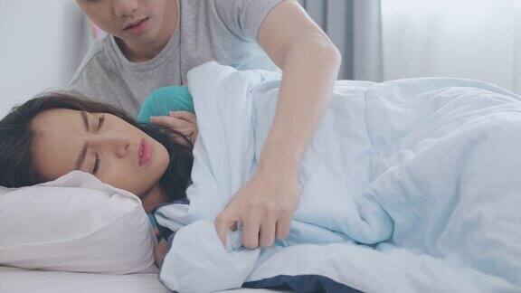 年轻的亚洲男子把温暖的毯子给他的女朋友在床上