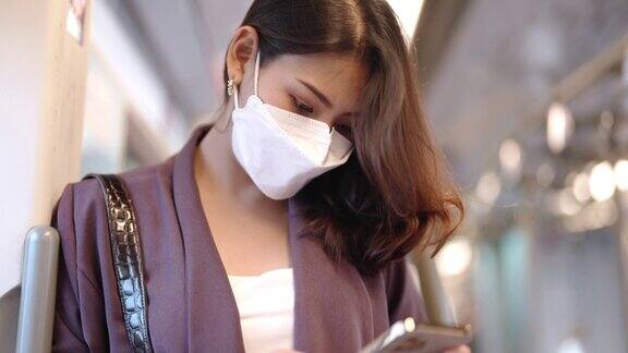 亚洲女商人在乘坐公共交通列车时戴着口罩一位女士站在窗前用智能手机看东西保护传染病和公共卫生