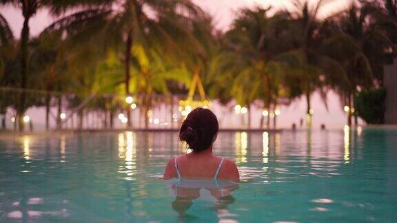 年轻的女旅行者放松和享受日落的热带度假胜地海滨游泳池而旅行暑假