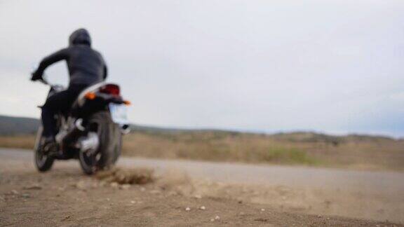 一个骑摩托车的人在尘土飞扬的路上从摩托车上开下来