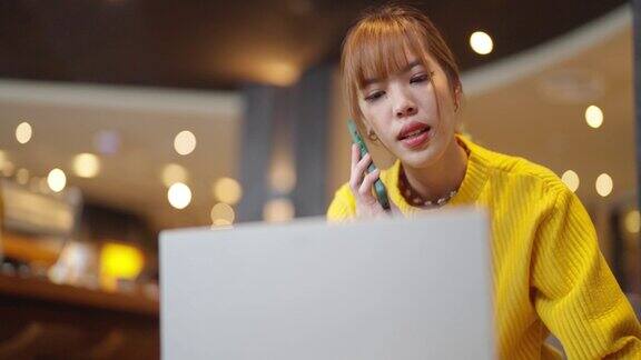 4K亚洲女性在咖啡馆用笔记本电脑工作用手机通话