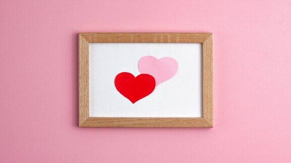 定格动画的粉红色和红色纸心木框架在粉红色的背景在中心边情人节母亲节爱情关系浪漫的纪念日概念平躺
