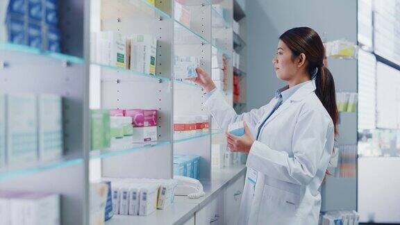 药店:美丽的亚洲药剂师穿着白大褂安排药包药盒维生素和补充药丸在柜台后面的架子上的肖像
