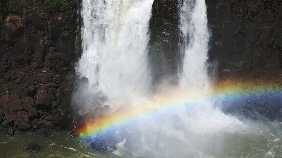 明亮美丽的彩虹被巨大的瀑布覆盖在伊瓜苏瀑布上巨大的水流从黑暗的岩石悬崖边缘落在巴西伊瓜苏瀑布的彩色彩虹拱门上