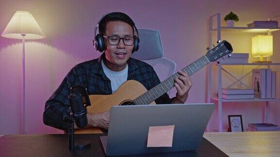 亚洲男子youtube直播表演弹吉他和唱一首歌亚洲人在网上教吉他和唱歌音乐家用笔记本电脑录制音乐演奏原声吉他