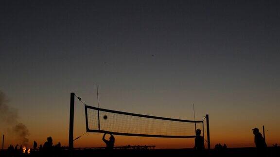 日落时分沙滩球场上排球网的剪影加利福尼亚海岸上的球员