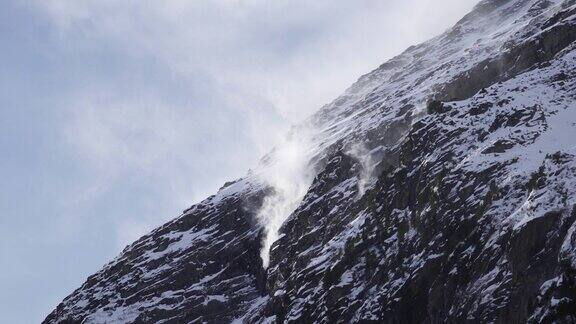 在多雪的岩石冰川斜坡上雪在山崖上被吹来吹去
