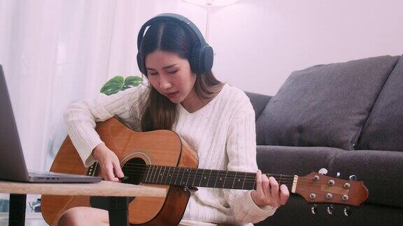 年轻女艺术家戴着耳机在家里学习原声吉他