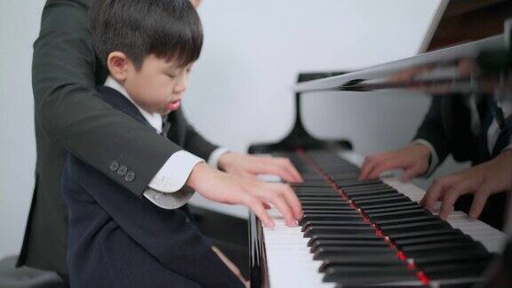 钢琴家在学校的教室里教一个男孩弹钢琴最喜欢的古典音乐在学习中快乐和乐趣身着正式优雅套装的音乐家教育、练习、放松的理念