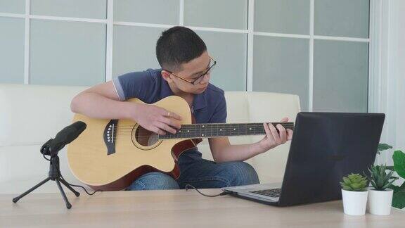 亚洲男孩弹奏吉他虚拟快乐时间会议在网上玩音乐与朋友在视频会议与笔记本电脑在网上会议在视频通话为社会距离