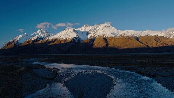 鸟瞰图飞过雪融化的河流朝向新西兰雪山的山峰