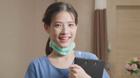 慢动作镜头中身着队服的女护士取下外科口罩看着镜头微笑美丽的亚洲年轻女工在医院微笑