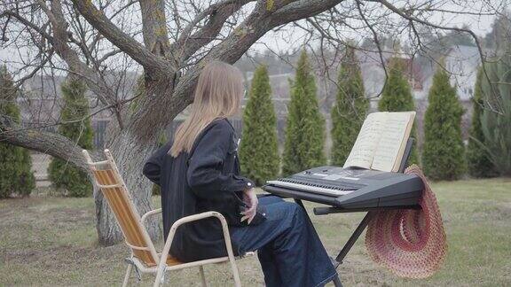 成功的专业可爱的钢琴家在后院的合成器上弹奏古典钢琴曲