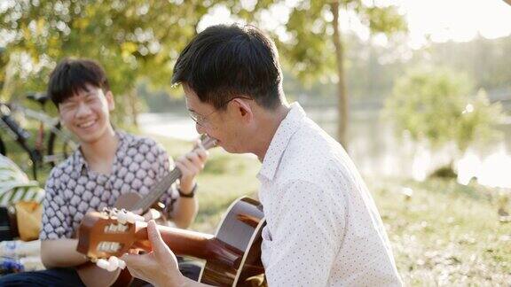 父子俩热情地练习吉他在惬意的夏日花园中愉快地放松亚洲家庭来野餐和演奏音乐长周末学习活动概念在一起自由