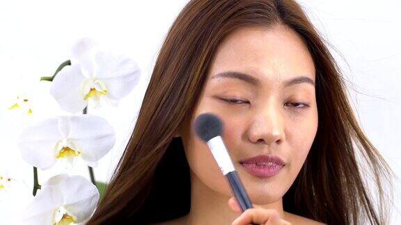大头照:亚洲美女用腮红刷化妆美丽的蝴蝶兰在白色的背景人以美容、保健、情感为理念