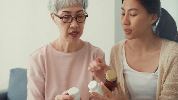 幸福的亚洲家庭年轻的女儿和年长的妈妈拿着药复合维生素瓶教年长的妈妈如何在家里吃药