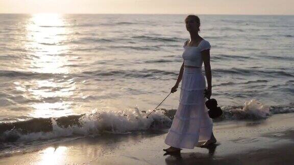 十几岁的女孩走在日落海滩上的小提琴