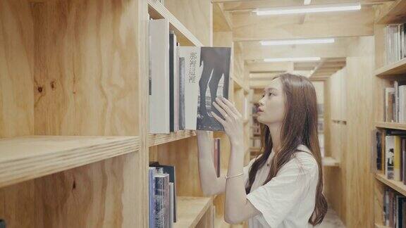 年轻的亚洲女大学生在图书馆找书(慢镜头)