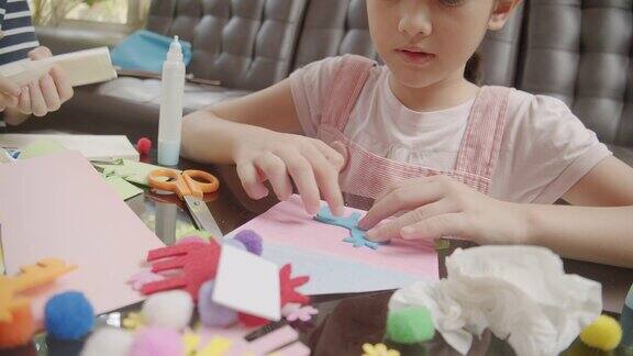 两个亚洲男孩和女孩在家的时候在客厅里剪纸和做工艺品他们用彩纸、剪刀和胶水在纸上创造艺术项目形成她的想象艺术和工艺概念