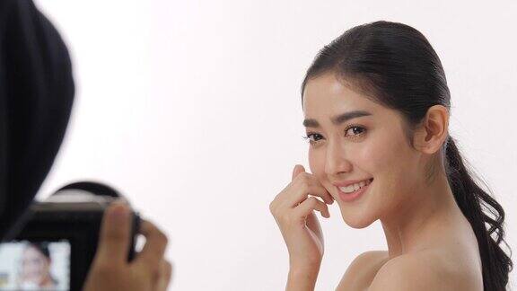 在幕后的美丽的年轻亚洲女性模特美丽的脸和完美的皮肤被记录在一个摄像机在一个白色的背景