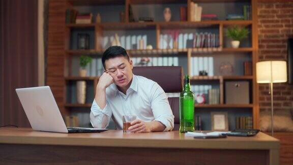 亚洲商人在办公室喝酒酗酒员工创业失败男人陷入绝望在工作场所的电脑桌前坐到很晚沮丧绝望和悲伤