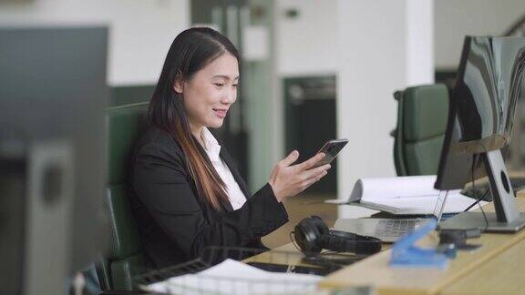 亚洲华人中年女性在开放式办公室工作时看智能手机视频通话