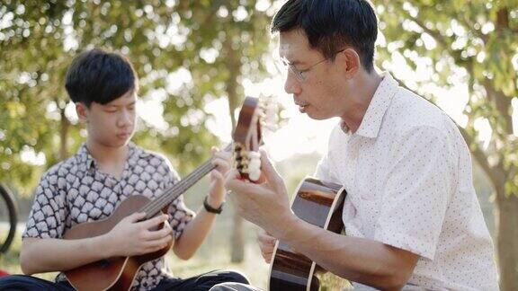 父子俩热情地练习吉他在惬意的夏日花园中愉快地放松亚洲家庭来野餐和演奏音乐长周末学习活动概念在一起自由