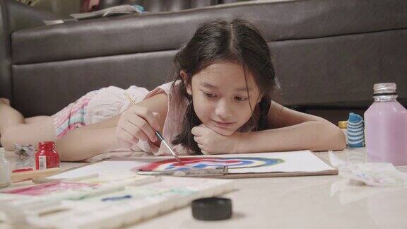 特写亚洲小女孩躺在地板上画画和绘画她的艺术和工艺在客厅而呆在家里她用水彩和画笔在白纸上创作艺术项目形成自己的想象艺术和工艺概念
