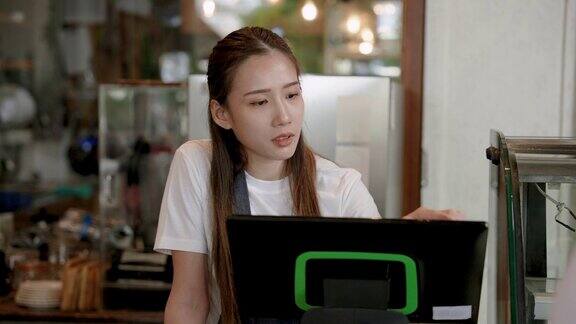美丽的亚洲女人拥有一家小型家庭咖啡馆在电脑收银机上核对订单从订购应用程序屏幕上为在线系统中订购的客户准备咖啡