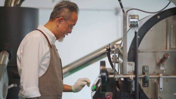 亚裔华裔技工操作咖啡烘焙机的控制面板触摸屏为咖啡烘焙过程做准备
