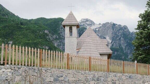 从下面看阿尔巴尼亚的教堂Theth白天阿尔卑斯山的背景上有雪木栅栏阴云密布