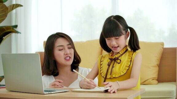 亚洲母亲帮助女儿在家里用笔记本电脑做作业