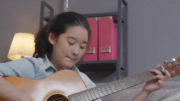 微笑的少女在家里的客厅弹吉他创造性的爱好