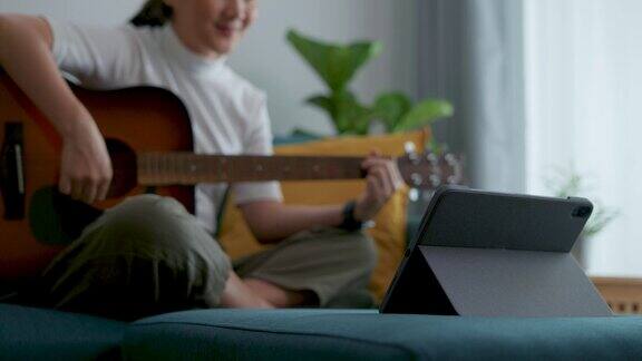 在家里的客厅里女人拿着吉他坐在沙发上用平板电脑学习吉他的特写镜头