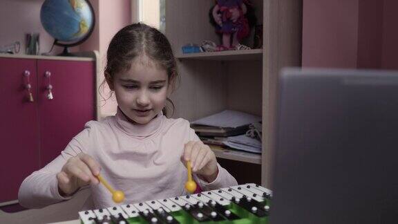 远程学习女生用笔记本电脑在线学习音乐课学生戴耳机观看网络音乐视频课程白人女孩学习弹奏木琴、钢琴