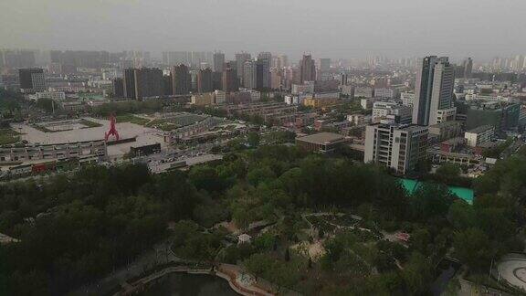 航拍无人机在城市公园和公共广场上空缓慢上升背景是城市