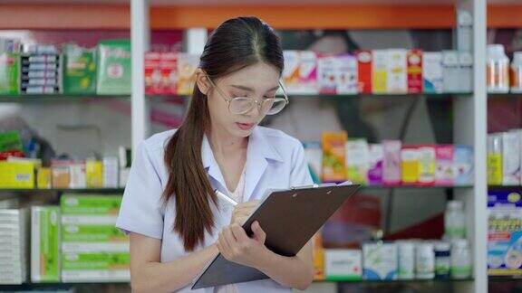 美丽的亚洲药剂师正在检查产品在现代药房哪个是有大量产品的零售商店