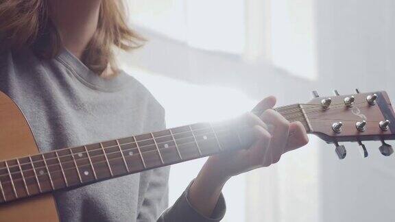 一个少年在阳光普照的白色客厅里弹吉他女人在室内作曲这位艺术家弹古典吉他一个女孩正在流行病期间独自练习一种乐器