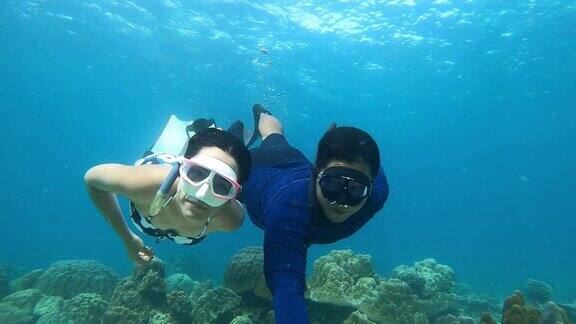 4K年轻的自由潜水员夫妇穿着长鳍和浮潜面具自拍潜水在美丽的珊瑚礁和鱼在大海清澈的水