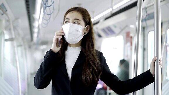 在新型冠状病毒感染的情况下年轻的亚洲女性戴着白色外科口罩在地铁上使用手机