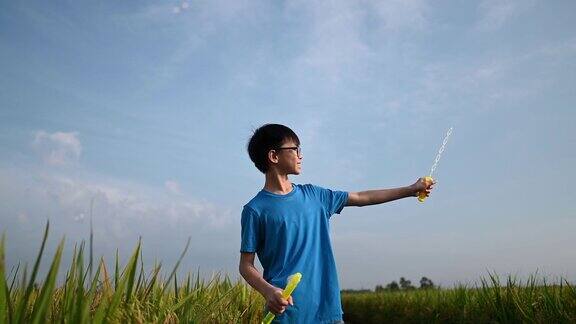 一个亚洲的中国男孩有一个有趣的周末在稻田与吹泡沫在早上
