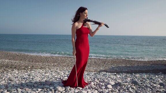 广角肖像苗条美丽的白人妇女穿着红色连衣裙站在阳光下的海岸小提琴和弓有才华的自信的女音乐家在地中海塞浦路斯