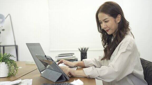 4K商务女性在办公室用笔记本电脑工作时使用数字平板电脑