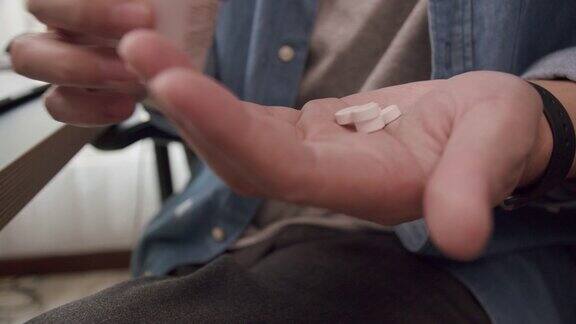 (特写)生病的亚洲男子在家里工作时手里拿着一粒白色药丸