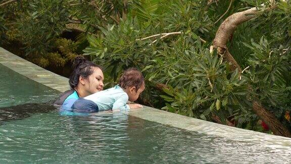 一位亚洲母亲带着她的儿子在巴厘岛的热带森林里享受室外无边泳池乌布印尼